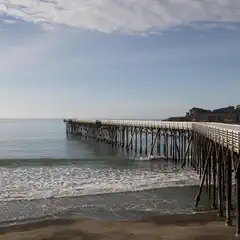 A long wooden pier extends into the ocean from a sandy beach.