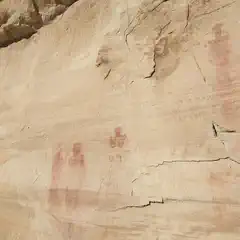 An ancient rock face features human figures painted in red.