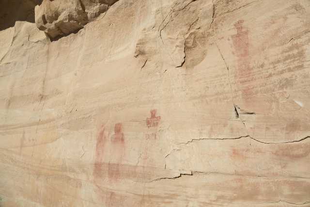 An ancient rock face features human figures painted in red.
