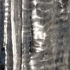 A close-up of icicles hanging from a structure, exhibiting intricate patterns and glimmering with light reflected off their surfaces.