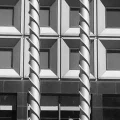 Two helical columns stand before a grid of recessed windows on a modern building facade.
