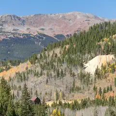 A mountainous landscape with autumn-colored trees and a small building near the bottom of the hill.