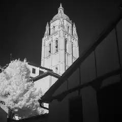 A tall cathedral tower with a pointed roof and arched windows, illuminated against a dark sky.