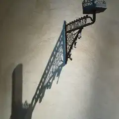 A wrought iron sconce casts a detailed shadow on a stucco wall.