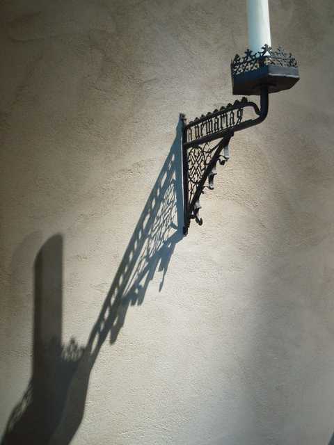 A wrought iron sconce casts a detailed shadow on a stucco wall.
