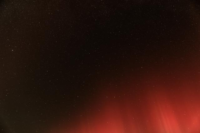 A night sky filled with stars, with a red glow on the horizon.