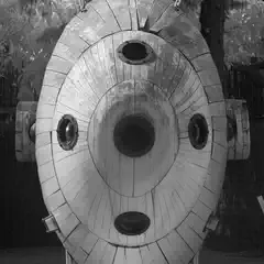 A wooden submarine-like structure with portholes and a central hatch is displayed outdoors, surrounded by trees and fencing.