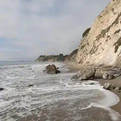 A sandy beach extends along a cliff face with ocean waves breaking on the shore.