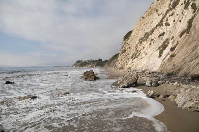 A sandy beach extends along a cliff face with ocean waves breaking on the shore.