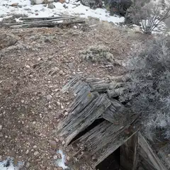 A crumbling wooden structure on rocky terrain with sparse vegetation and patches of snow.
