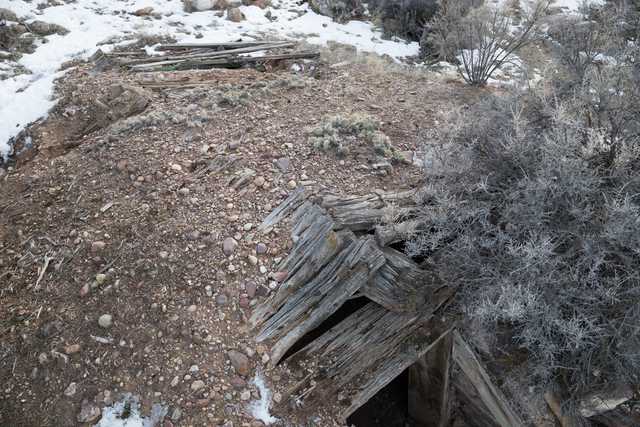A crumbling wooden structure on rocky terrain with sparse vegetation and patches of snow.