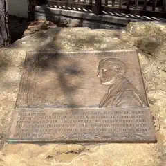 A bronze plaque with a relief portrait and text is mounted on a large, rough stone.