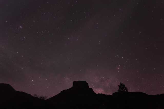 A night sky filled with stars, highlighted by the Milky Way galaxy, set against silhouetted mountain peaks.