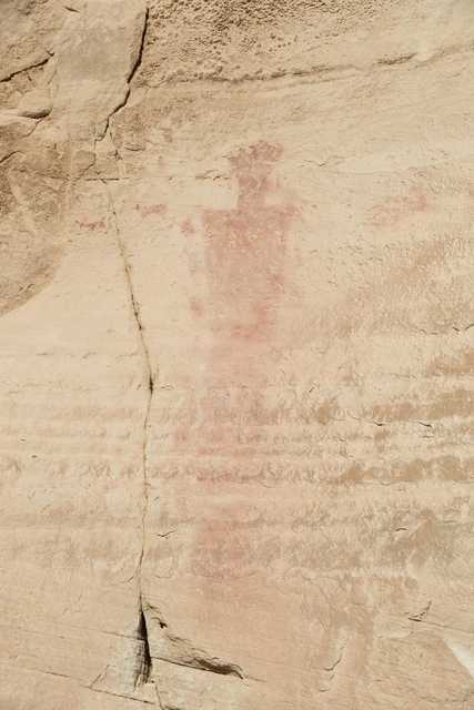 An ancient red pictograph on a light-colored rock surface, depicting a human figure.
