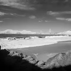 A beach extends toward a distant bridge with mountains in the background.