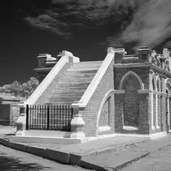 A brick mausoleum has a staircase leading up to its entrance.