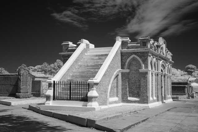 A brick mausoleum has a staircase leading up to its entrance.