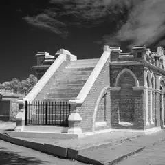 A brick mausoleum has a staircase leading up to its entrance.