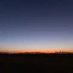 A city skyline at dusk with a bridge and tower silhouetted against the fading light of day.