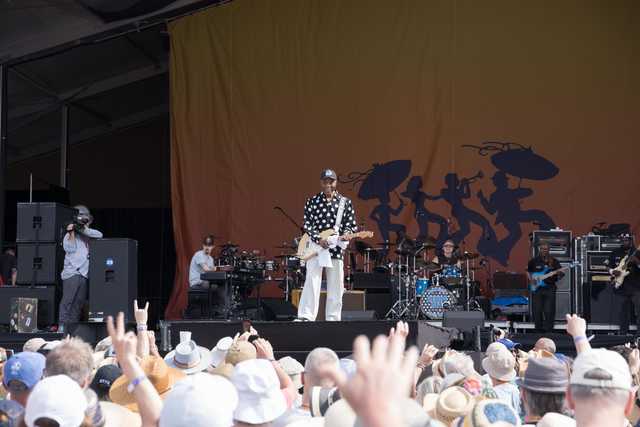 A crowd of people with raised hands and cameras, watching a man on stage playing a guitar, at an outdoor event.
