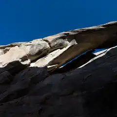 A sandstone rock formation is set against a backdrop of a blue sky and the moon in the distance.
