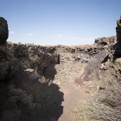 A rugged, volcanic landscape with jagged rock formations and deep crevices, under a clear blue sky.