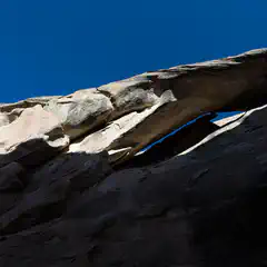 A sandstone rock formation is set against a backdrop of a blue sky and the moon in the distance.
