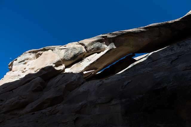 A sandstone rock formation is set against a backdrop of a blue sky and the moon in the distance.