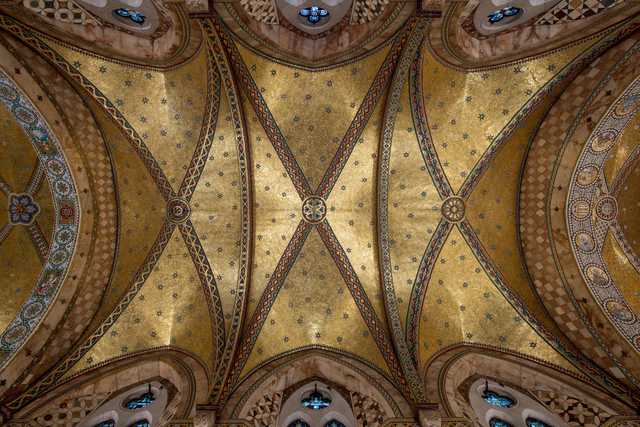 A vaulted ceiling adorned with intricate gold mosaics, geometric patterns, and colorful stained glass windows.