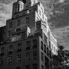 A tall building with numerous windows and setbacks under a cloudy sky.