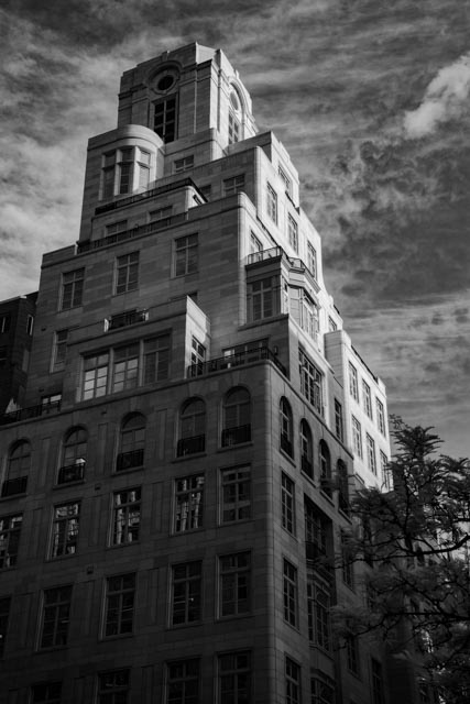 A tall building with numerous windows and setbacks under a cloudy sky.