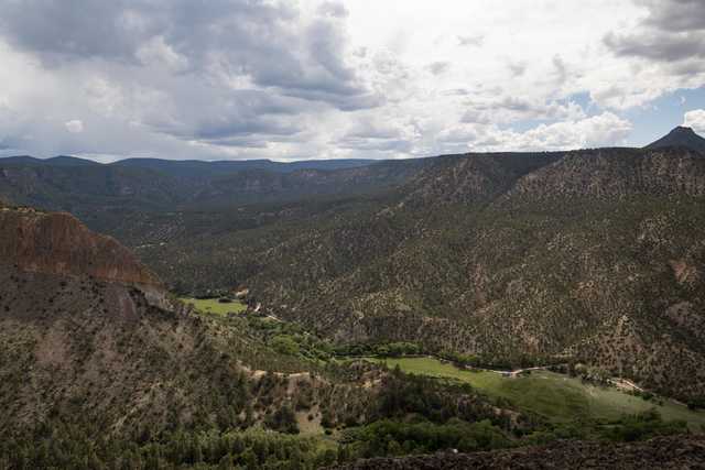 A mountainous landscape features a valley with trees and grass, surrounded by rocky terrain.
