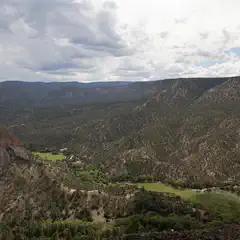A mountainous landscape features a valley with trees and grass, surrounded by rocky terrain.