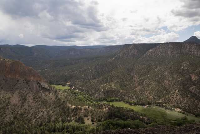 A mountainous landscape features a valley with trees and grass, surrounded by rocky terrain.