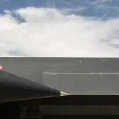 A dark aircraft extends into the frame against a blue sky with scattered clouds.