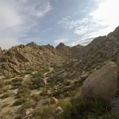 A rugged hillside with large boulders and sparse vegetation under a partly cloudy sky.