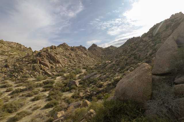 A rugged hillside with large boulders and sparse vegetation under a partly cloudy sky.