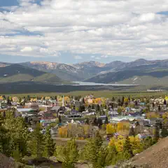 A small town surrounded by mountains and a lake, with autumnal hues of yellow and green visible in the landscape.