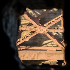 A red bridge with metal grid and arches seen through a small window in a stone wall.