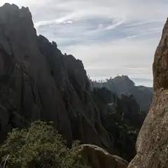 A rugged landscape of towering rock formations and sparse vegetation stretches into the distance under a partly cloudy sky.