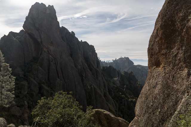 A rugged landscape of towering rock formations and sparse vegetation stretches into the distance under a partly cloudy sky.