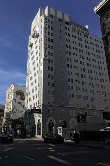 A tall building with many windows stands on a city street.