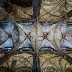 A stone ceiling features arched vaults separated by ribbed gothic arches, with a light-colored brick pattern on the underside.