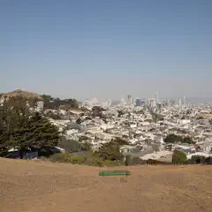 A bench sits on a hill overlooking a densely populated urban area.