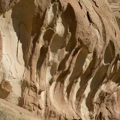 A sandstone cliff face features deep grooves that have been eroded by the wind or water over time.