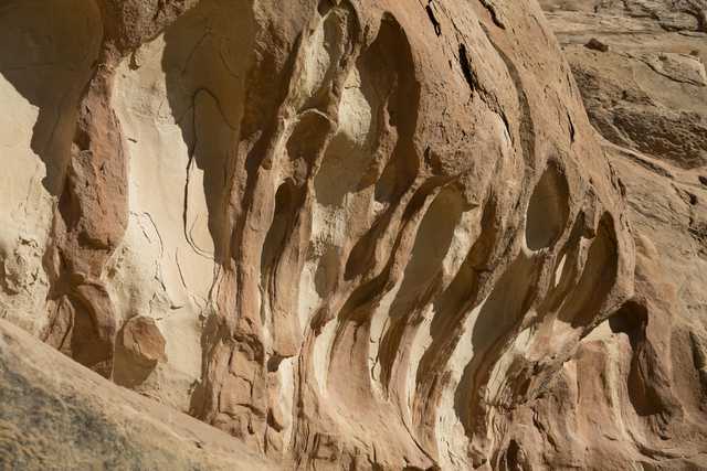 A sandstone cliff face features deep grooves that have been eroded by the wind or water over time.