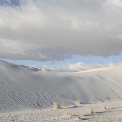 An expanse of white sand dunes stretches across the landscape under a blue sky with clouds.