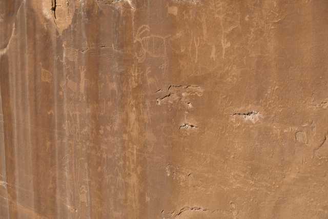 A smooth, red sandstone cliff face covered with dozens of petroglyphs.