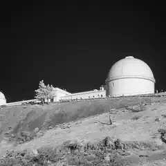 A white dome on top of a hill, with another smaller dome to its left and a long building behind them.
