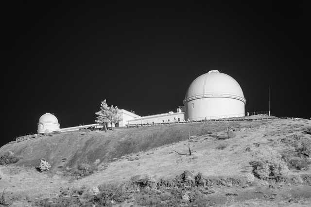 A white dome on top of a hill, with another smaller dome to its left and a long building behind them.